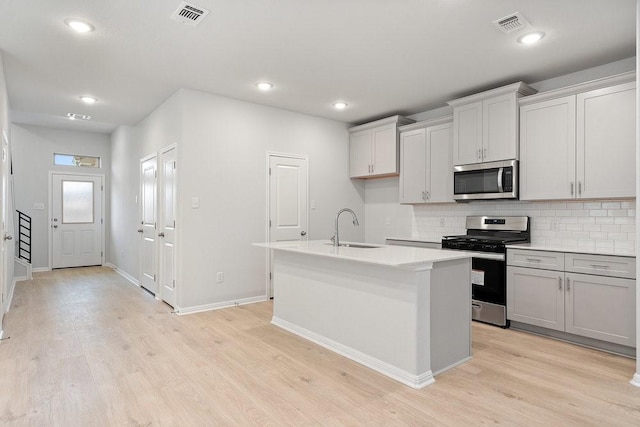 kitchen featuring backsplash, sink, light wood-type flooring, an island with sink, and stainless steel appliances