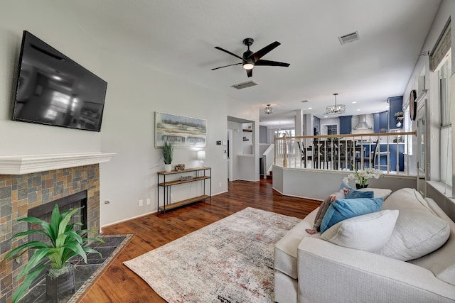 living room featuring ceiling fan with notable chandelier, dark wood-type flooring, and a tiled fireplace