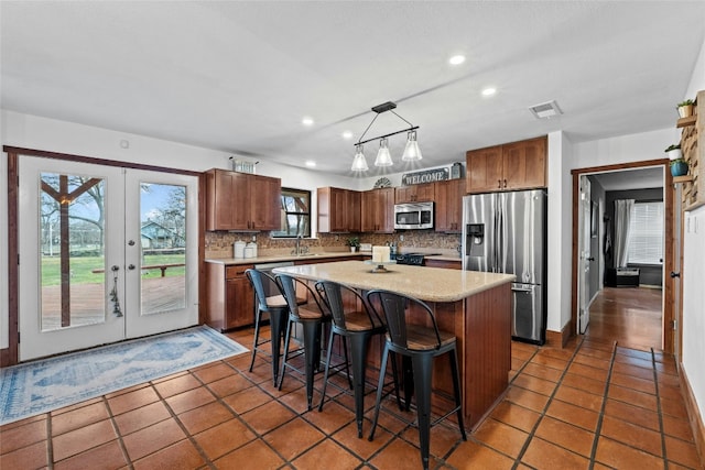 kitchen featuring french doors, a breakfast bar, stainless steel appliances, pendant lighting, and a center island