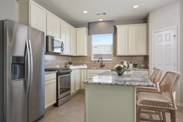 kitchen with appliances with stainless steel finishes, light stone counters, sink, a center island, and a breakfast bar area