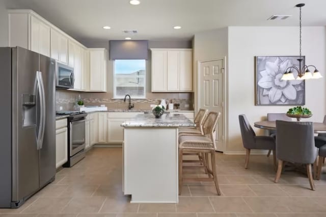 kitchen with stainless steel appliances, pendant lighting, a notable chandelier, white cabinets, and a kitchen island