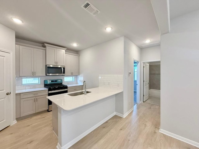 kitchen with decorative backsplash, kitchen peninsula, sink, and appliances with stainless steel finishes