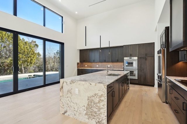 kitchen featuring sink, tasteful backsplash, high end fridge, double wall oven, and a center island with sink