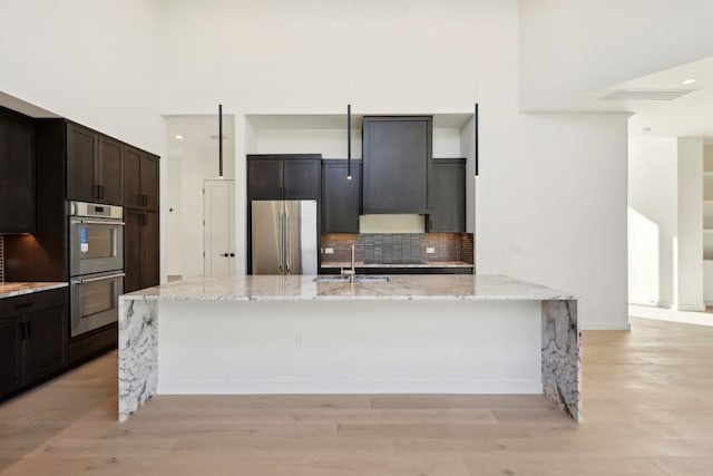 kitchen with appliances with stainless steel finishes, light stone counters, a kitchen island with sink, and sink