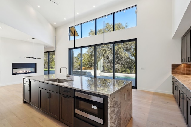 kitchen with light stone countertops, built in microwave, sink, decorative light fixtures, and a high ceiling