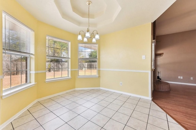 tiled spare room featuring a notable chandelier and a tray ceiling