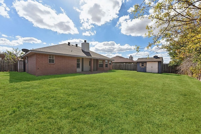 back of house featuring a fenced backyard, a yard, a shed, an outdoor structure, and brick siding