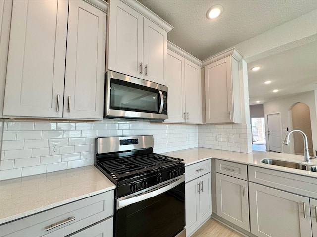 kitchen featuring sink, light stone counters, a textured ceiling, appliances with stainless steel finishes, and backsplash