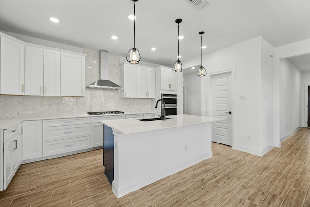 kitchen with white cabinetry, sink, wall chimney range hood, and an island with sink