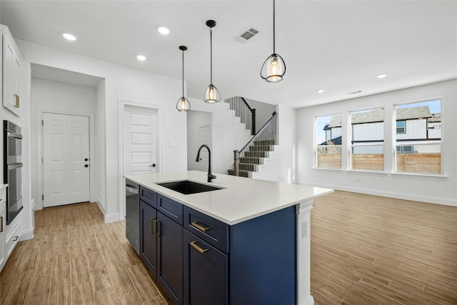 kitchen with a center island with sink, sink, light wood-type flooring, decorative light fixtures, and white cabinetry