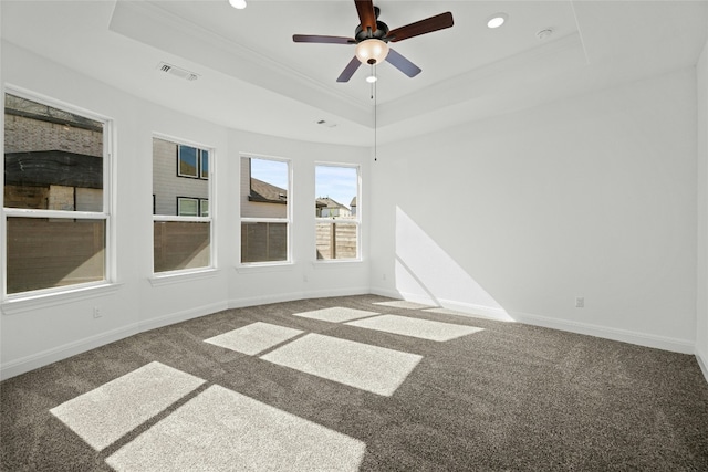 spare room with a tray ceiling, ceiling fan, and dark colored carpet