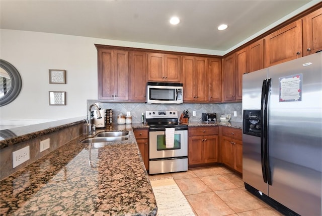 kitchen featuring sink, backsplash, dark stone countertops, light tile patterned floors, and appliances with stainless steel finishes