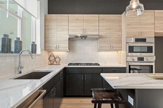 kitchen with light stone countertops, sink, decorative light fixtures, a kitchen bar, and appliances with stainless steel finishes