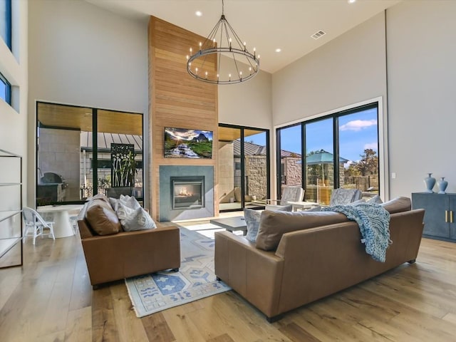 living room with a fireplace, a chandelier, a high ceiling, and light hardwood / wood-style flooring