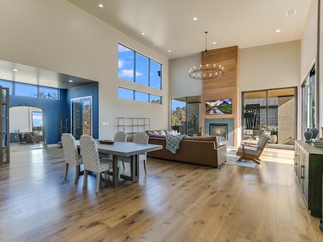 dining room featuring a fireplace, a towering ceiling, light hardwood / wood-style floors, and an inviting chandelier