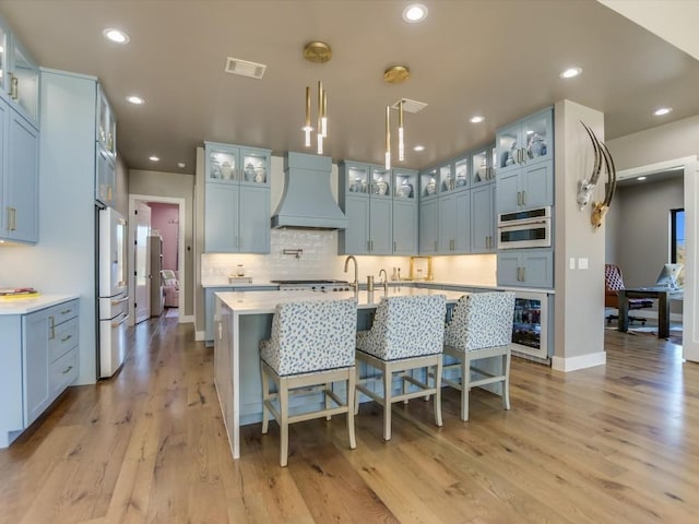 kitchen featuring premium range hood, wine cooler, light hardwood / wood-style floors, and an island with sink