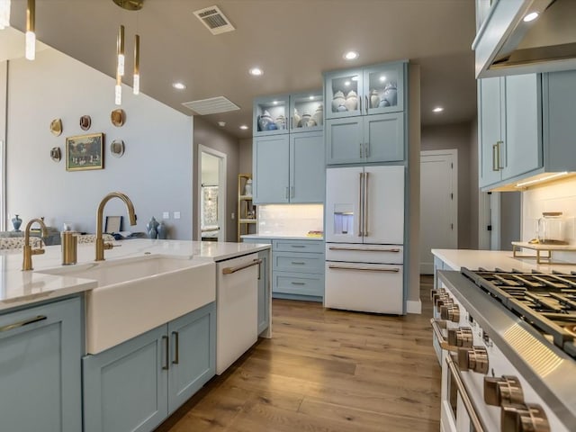 kitchen featuring light stone countertops, white appliances, decorative light fixtures, light hardwood / wood-style floors, and range hood