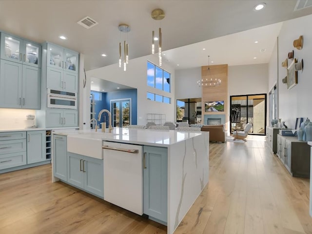 kitchen with a towering ceiling, white appliances, a kitchen island with sink, sink, and pendant lighting