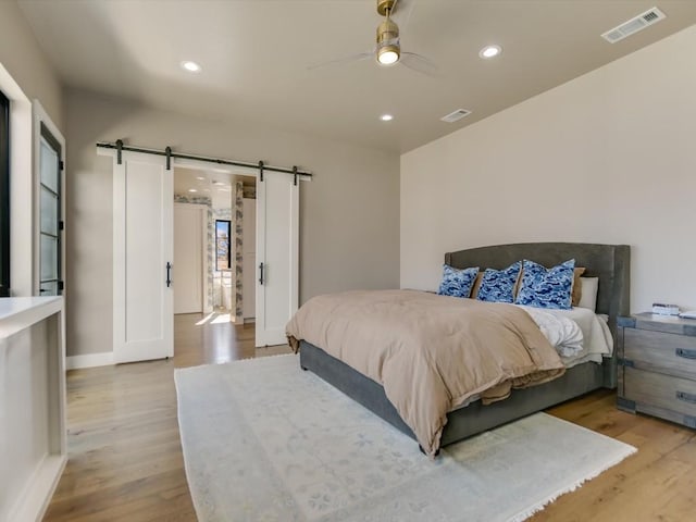 bedroom with a barn door, light hardwood / wood-style floors, ensuite bath, and ceiling fan