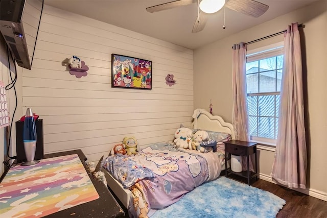 bedroom featuring dark hardwood / wood-style flooring, ceiling fan, and wood walls