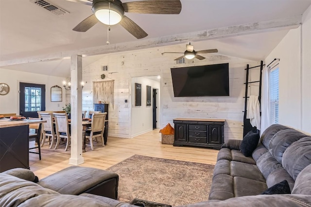 living room with ceiling fan with notable chandelier, light wood-type flooring, lofted ceiling with beams, and wood walls