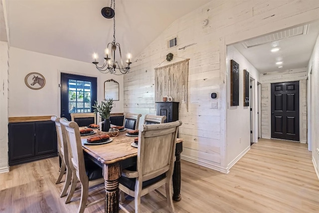 dining area featuring a chandelier, light hardwood / wood-style flooring, vaulted ceiling, and wooden walls