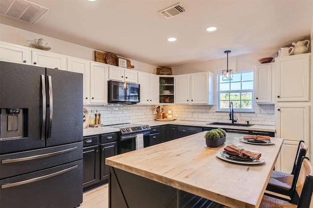 kitchen featuring fridge with ice dispenser, sink, decorative light fixtures, stainless steel electric range, and a breakfast bar area