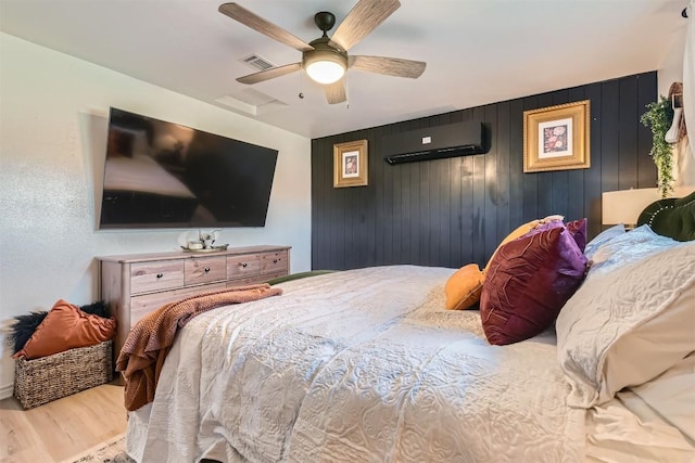 bedroom with wood walls, light hardwood / wood-style flooring, ceiling fan, and a wall mounted air conditioner