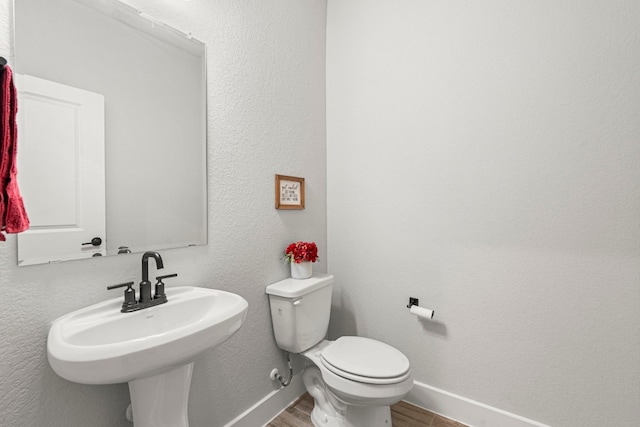 bathroom with toilet, wood finished floors, baseboards, and a sink