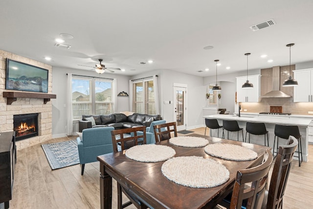 dining space with a ceiling fan, a fireplace, visible vents, and light wood finished floors