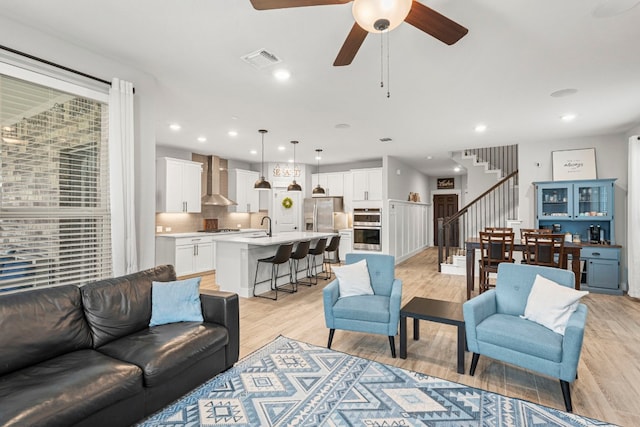 living area with stairs, a ceiling fan, visible vents, and light wood-type flooring