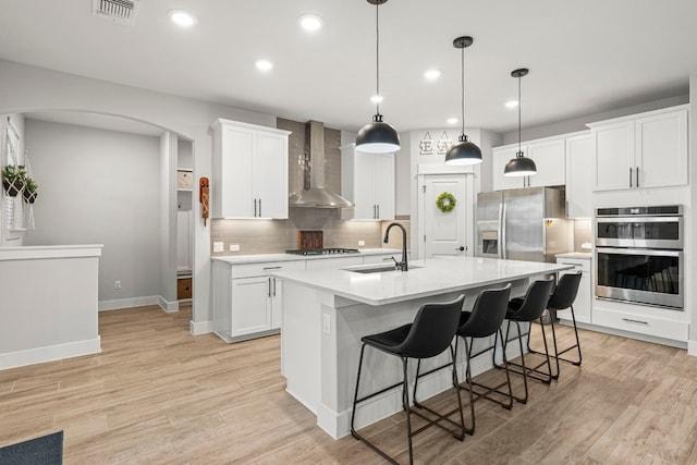 kitchen with visible vents, a sink, stainless steel appliances, arched walkways, and wall chimney exhaust hood