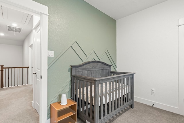 bedroom with visible vents, a crib, attic access, and carpet floors