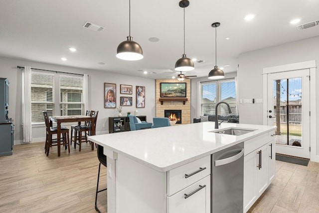 kitchen featuring visible vents, dishwasher, a fireplace, and a sink