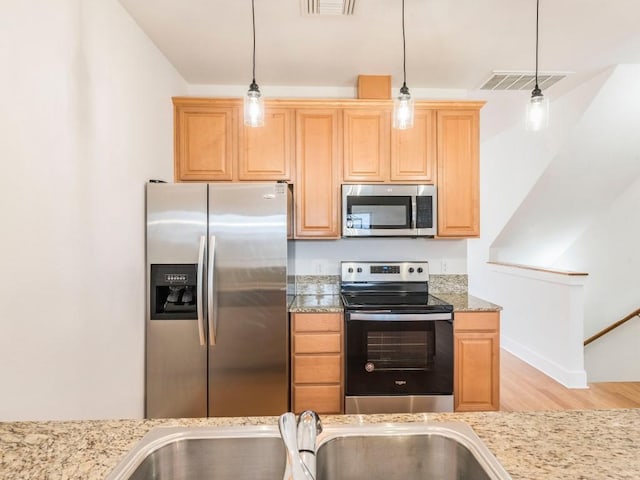 kitchen featuring light stone countertops, sink, light hardwood / wood-style flooring, decorative light fixtures, and appliances with stainless steel finishes