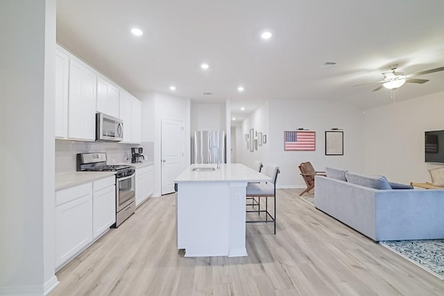 kitchen with a sink, a kitchen breakfast bar, open floor plan, appliances with stainless steel finishes, and light wood-type flooring