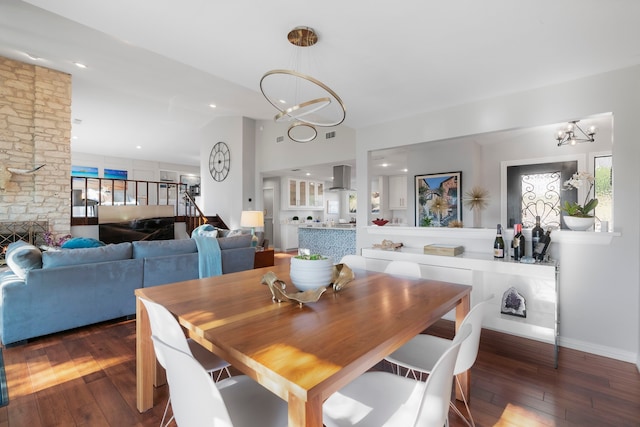 dining area featuring an inviting chandelier, a stone fireplace, and dark hardwood / wood-style flooring