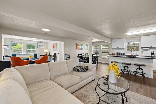 living area featuring baseboards, visible vents, light wood-style flooring, and a textured ceiling