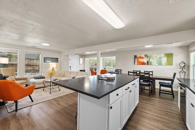 kitchen featuring a kitchen island, white cabinetry, a kitchen bar, dark wood-type flooring, and a textured ceiling