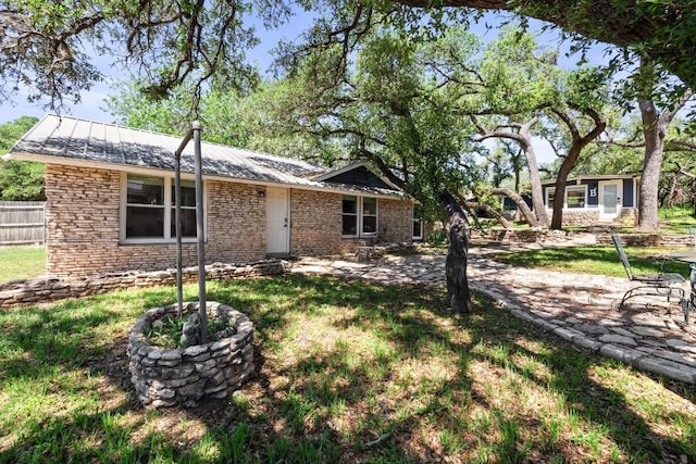 view of front of house featuring metal roof, fence, stone siding, a standing seam roof, and a front yard