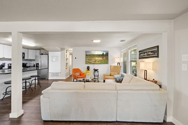 living area featuring dark wood-type flooring, visible vents, a textured ceiling, and baseboards