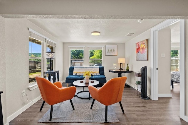 sitting room with a textured ceiling, dark wood-type flooring, visible vents, and a healthy amount of sunlight