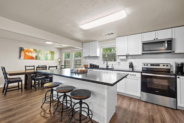 kitchen with stainless steel appliances, dark countertops, visible vents, white cabinets, and a kitchen island