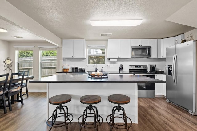 kitchen with dark countertops, a center island, stainless steel appliances, a kitchen bar, and white cabinetry