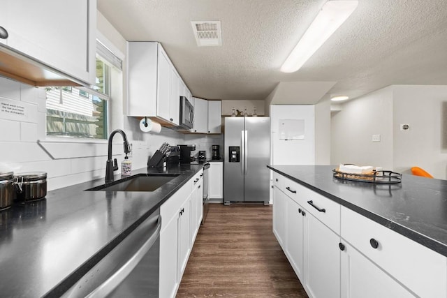 kitchen featuring visible vents, dark countertops, stainless steel appliances, white cabinetry, and a sink