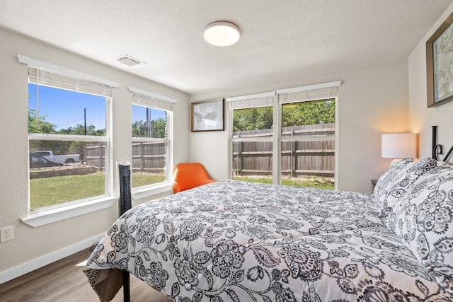 bedroom featuring baseboards, a textured ceiling, visible vents, and wood finished floors