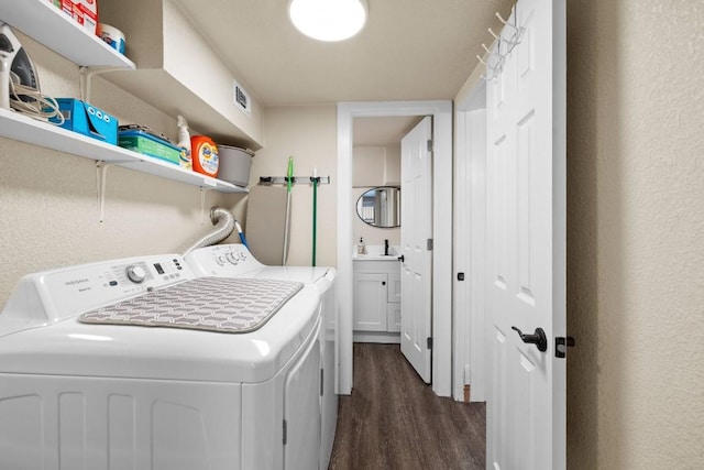 laundry area featuring dark wood-style floors, a textured wall, a sink, and separate washer and dryer