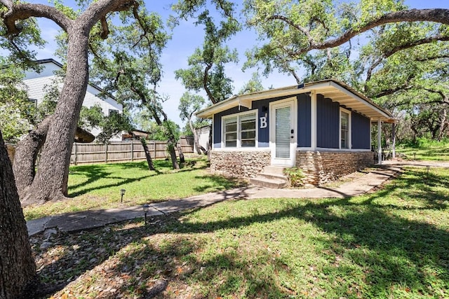 view of front of property with entry steps, fence, stone siding, board and batten siding, and a front yard