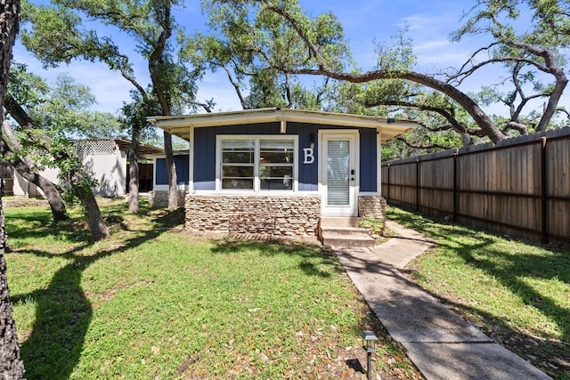 view of front facade featuring entry steps, stone siding, fence, board and batten siding, and a front yard