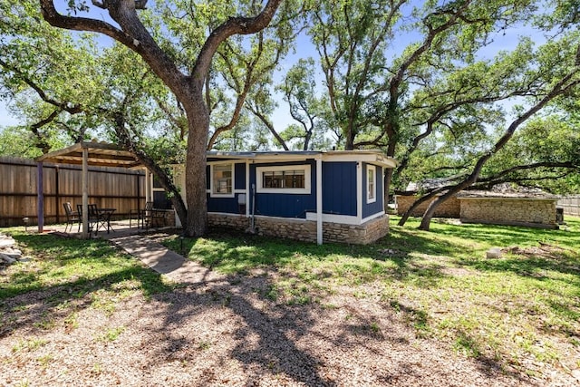 rear view of property featuring stone siding, fence, board and batten siding, and a yard